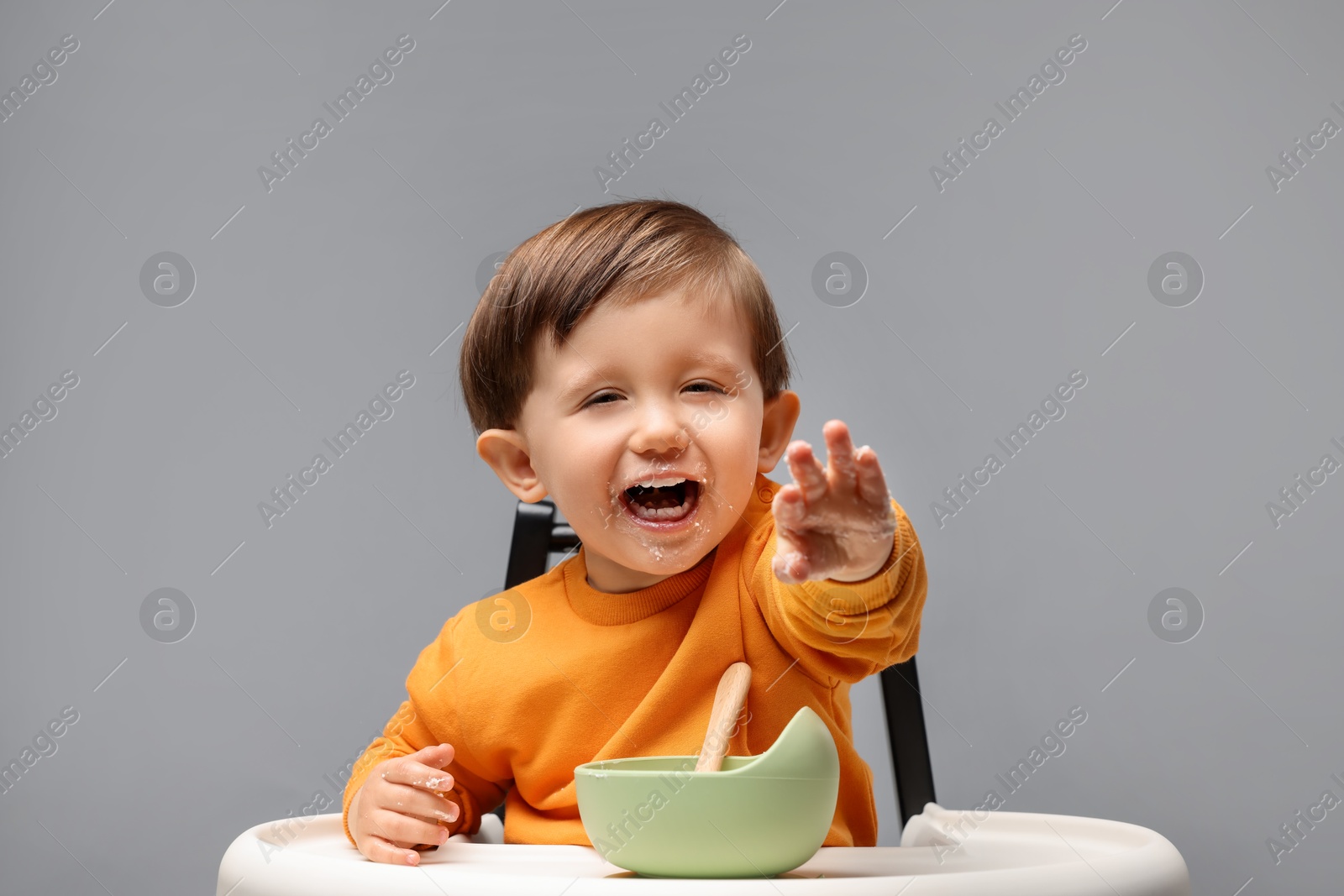 Photo of Cute little kid eating healthy baby food from bowl in high chair on light grey background