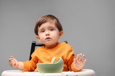 Photo of Cute little kid eating healthy baby food from bowl in high chair on light grey background