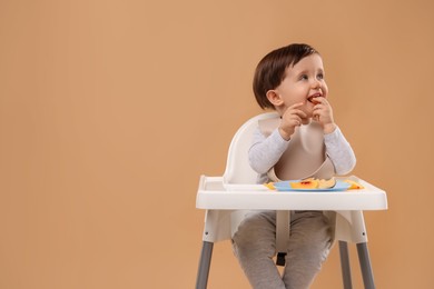 Photo of Healthy baby food. Cute little kid eating fruits in high chair on beige background, space for text