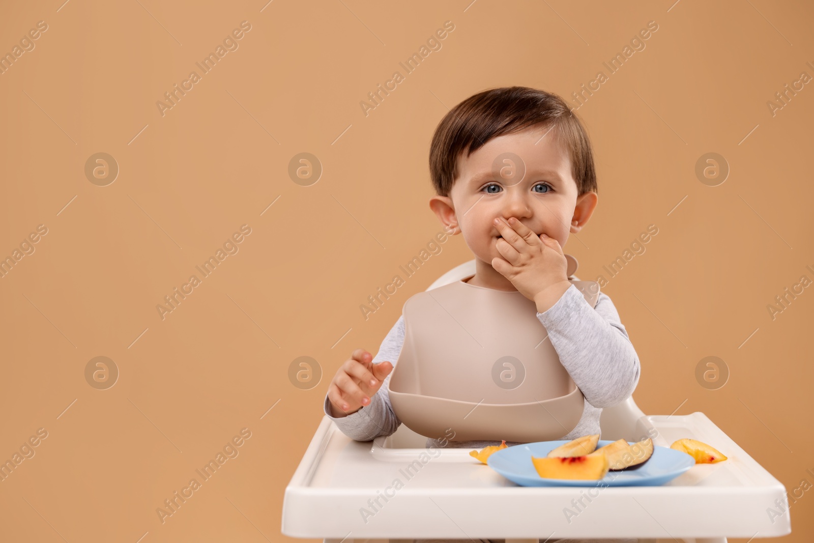 Photo of Healthy baby food. Cute little kid eating fruits in high chair on beige background, space for text