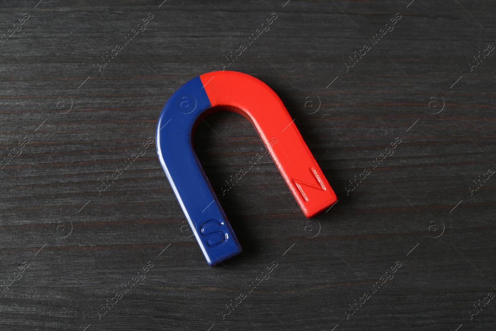 Photo of One horseshoe magnet on black wooden background, top view