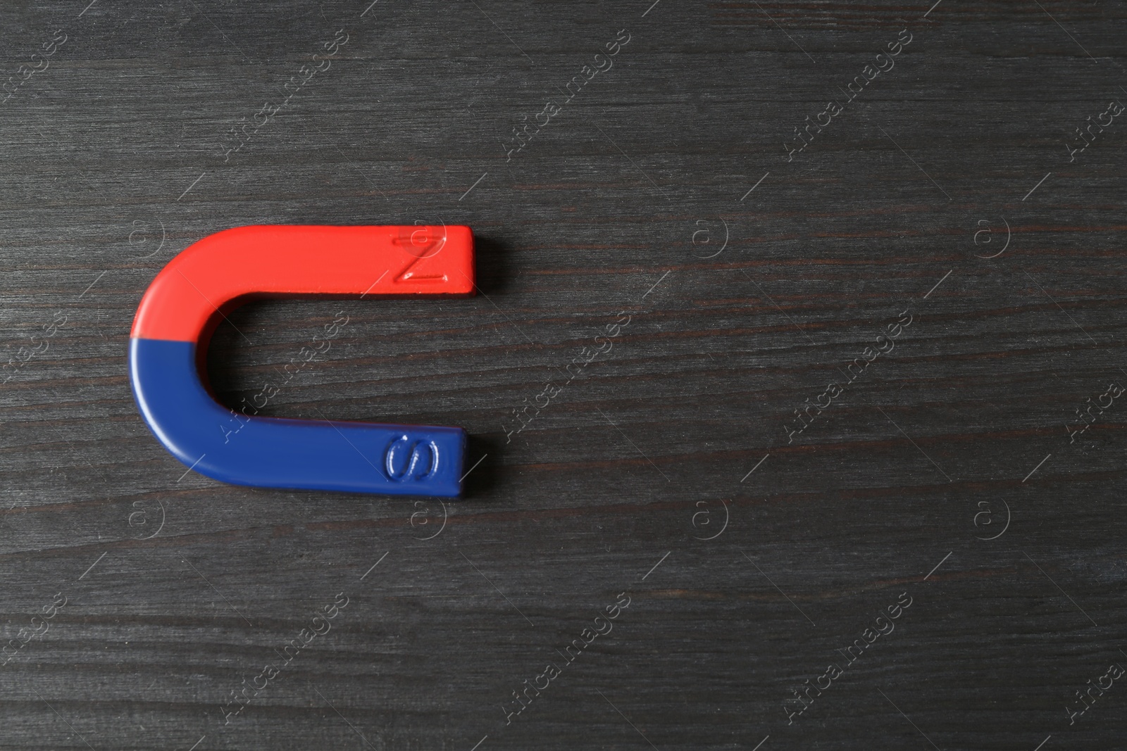 Photo of One horseshoe magnet on black wooden background, top view. Space for text