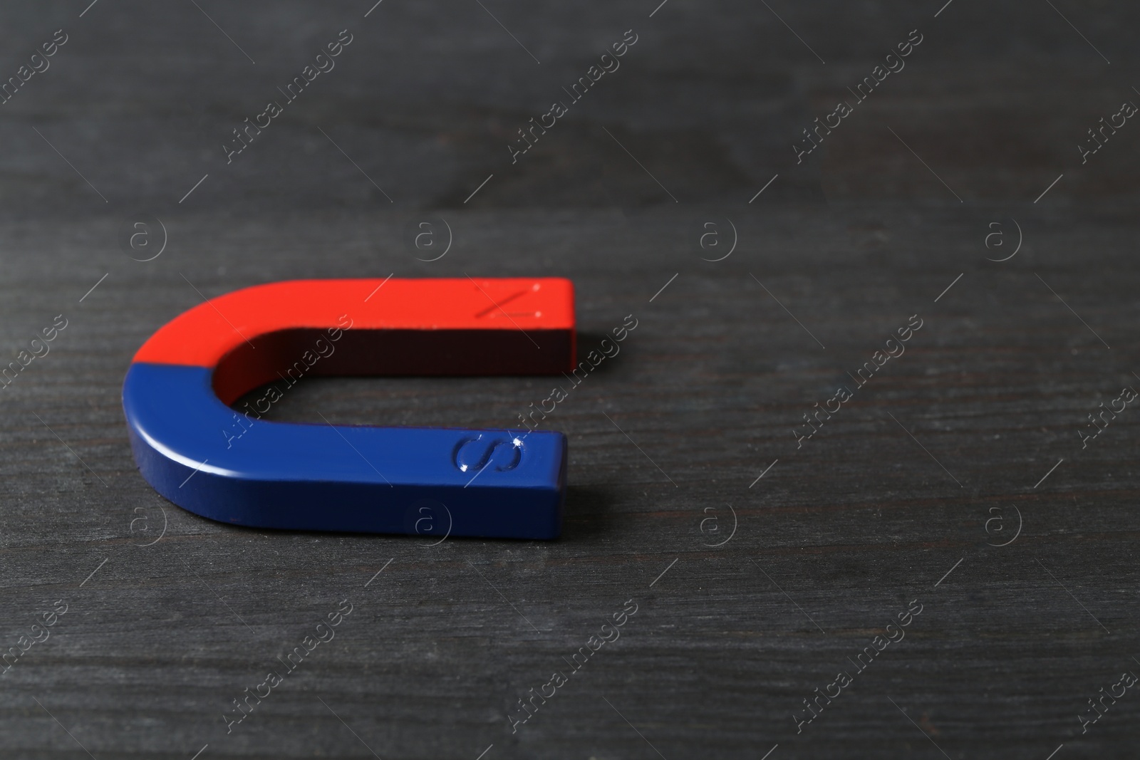 Photo of One horseshoe magnet on black wooden table, closeup. Space for text