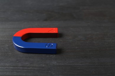 Photo of One horseshoe magnet on black wooden table, closeup. Space for text