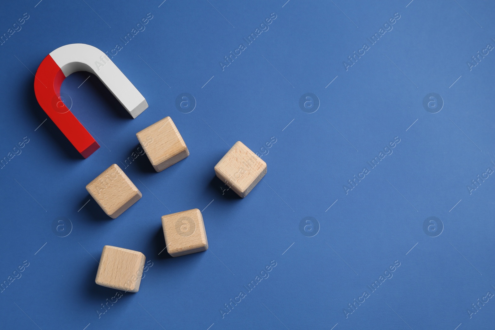 Photo of Magnet attracting wooden cubes on blue background, top view. Space for text