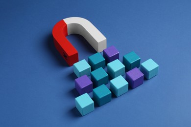 Photo of Magnet attracting colorful cubes on blue background