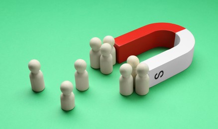 Photo of Magnet attracting human figures on green background, closeup