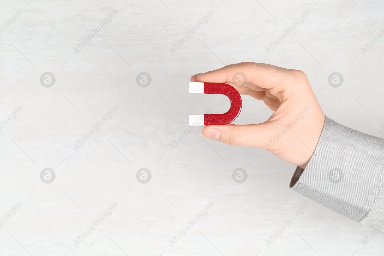 Photo of Woman with horseshoe magnet on light background, closeup. Space for text