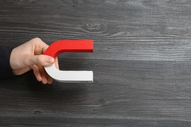 Photo of Woman with horseshoe magnet on wooden background, top view. Space for text