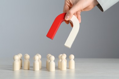 Photo of Woman with magnet attracting wooden human figures at light table, closeup