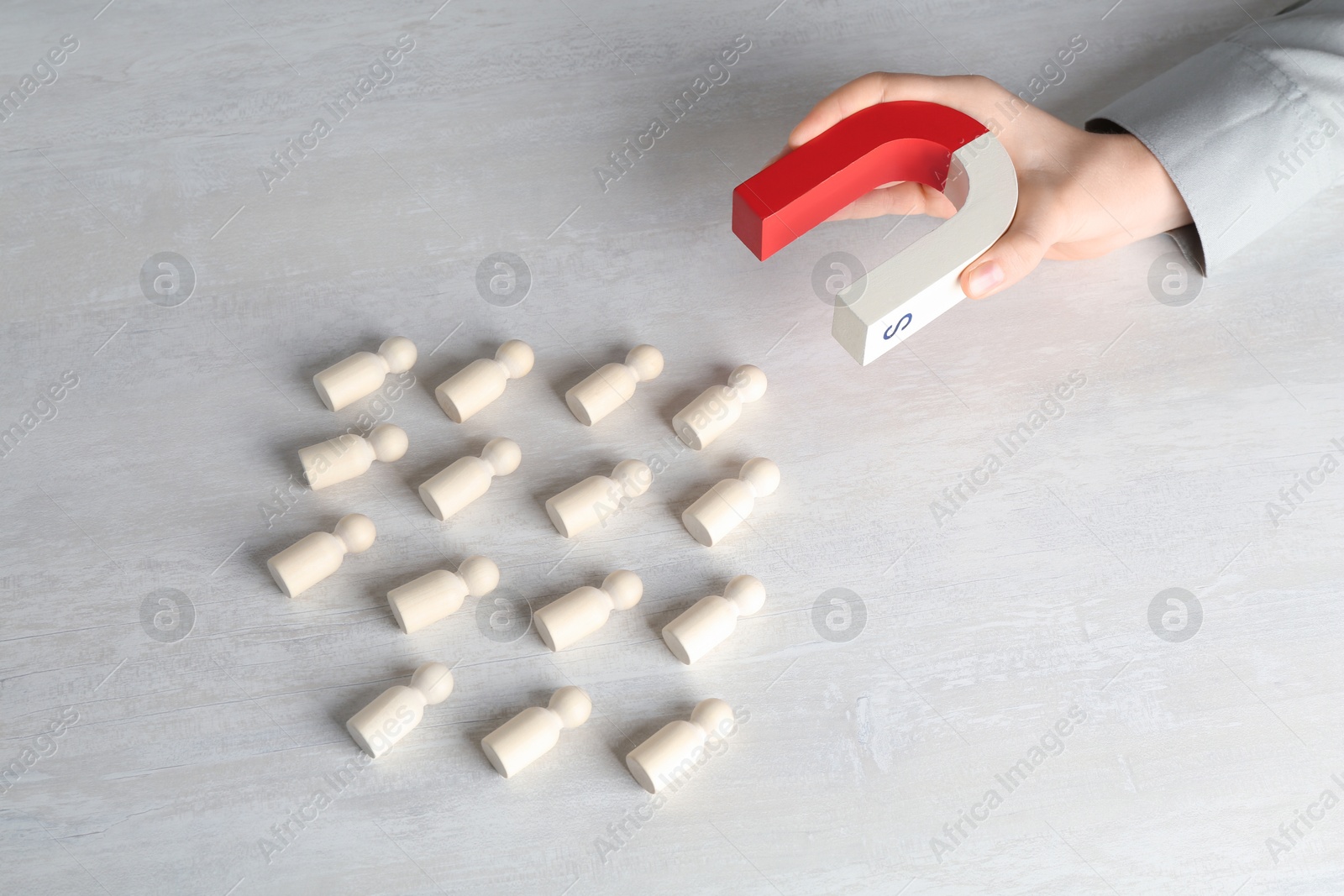 Photo of Woman with magnet attracting wooden human figures at light table, above view