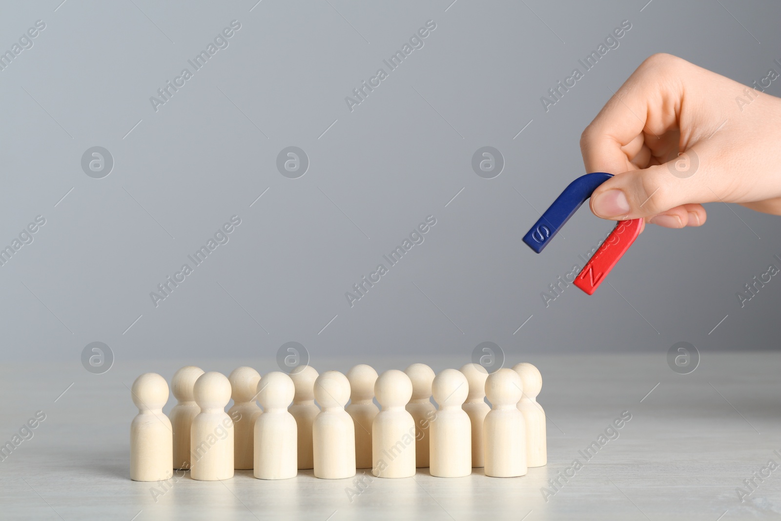 Photo of Woman with magnet attracting wooden human figures at light table, closeup