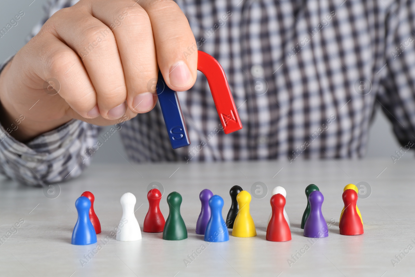 Photo of Man with magnet attracting colorful game pieces at light table, closeup