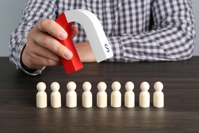 Photo of Man with magnet attracting human figures at wooden table, closeup