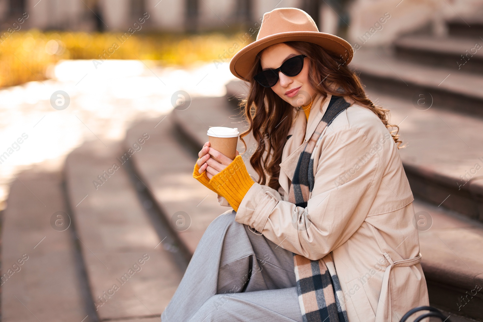 Photo of Charming young woman with cup of coffee on city street, space for text. Autumn season