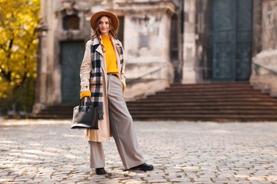 Photo of Charming young woman in stylish outfit on city street, space for text. Autumn season