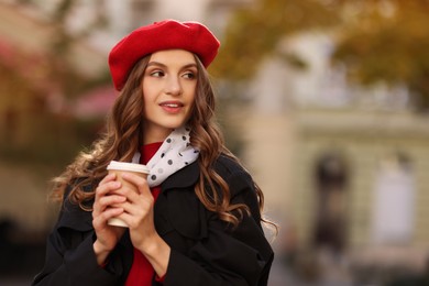 Stylish woman with cup of hot drink outdoors, space for text