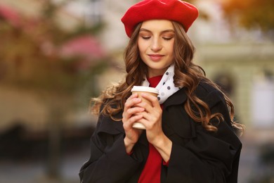 Photo of Stylish woman with cup of hot drink outdoors, space for text