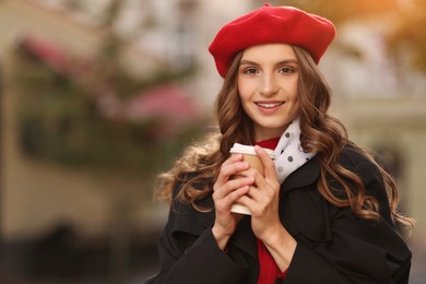 Photo of Stylish woman with cup of hot drink outdoors, space for text