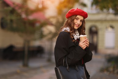 Photo of Stylish woman with cup of hot drink outdoors, space for text