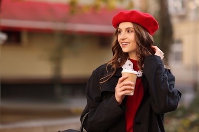 Stylish woman with cup of hot drink outdoors, space for text