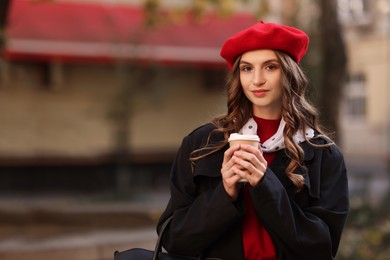 Photo of Stylish woman with cup of hot drink outdoors, space for text