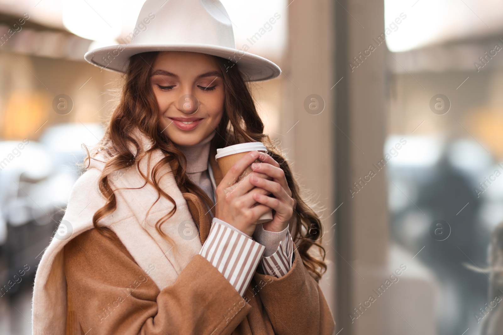 Photo of Charming young woman with hot drink near shop on city street, space for text