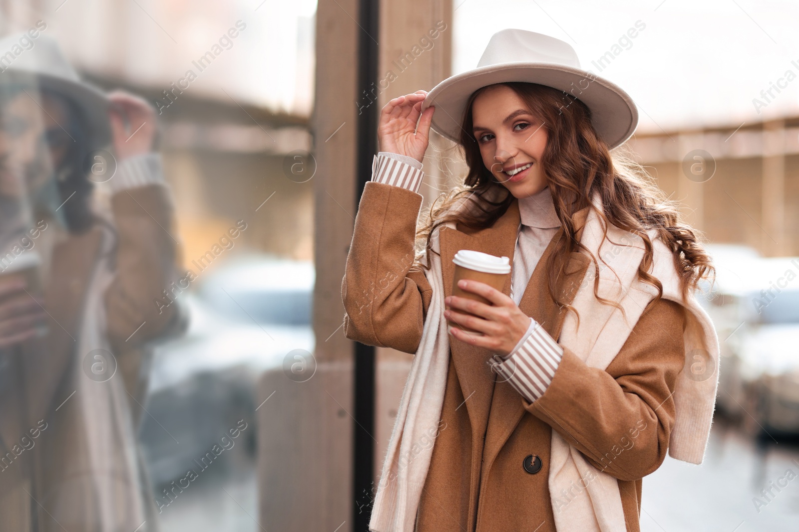 Photo of Charming young woman with hot drink near shop on city street