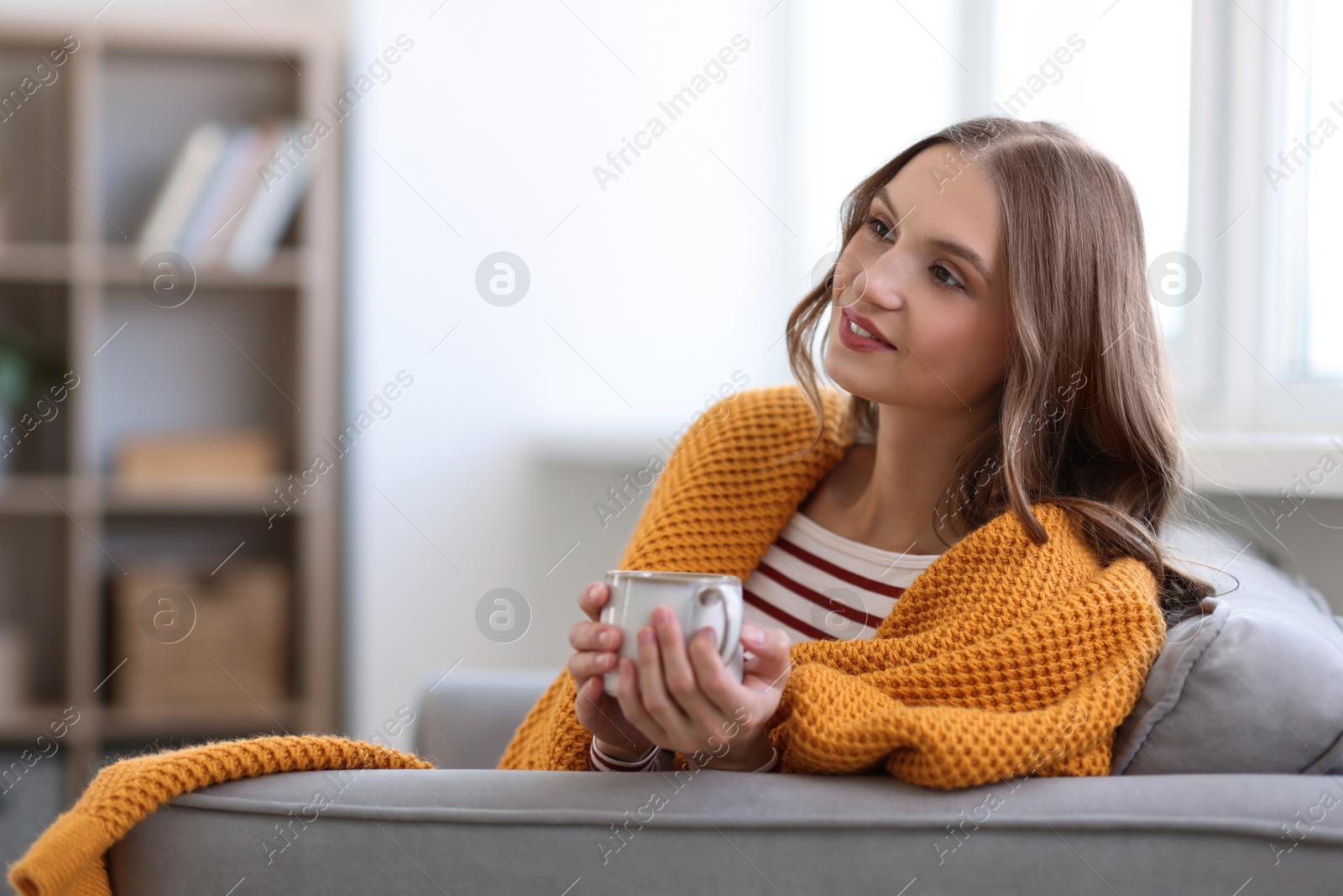 Photo of Charming young woman with cup of hot drink on sofa at home, space for text. Autumn atmosphere