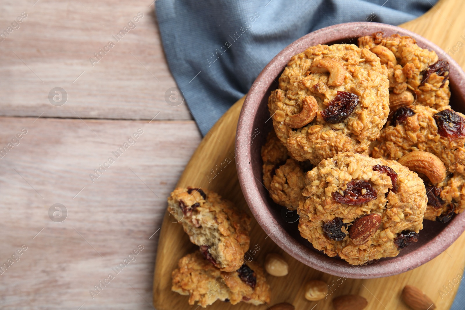 Photo of Delicious oatmeal cookies with raisins and nuts on wooden table, top view. Space for text