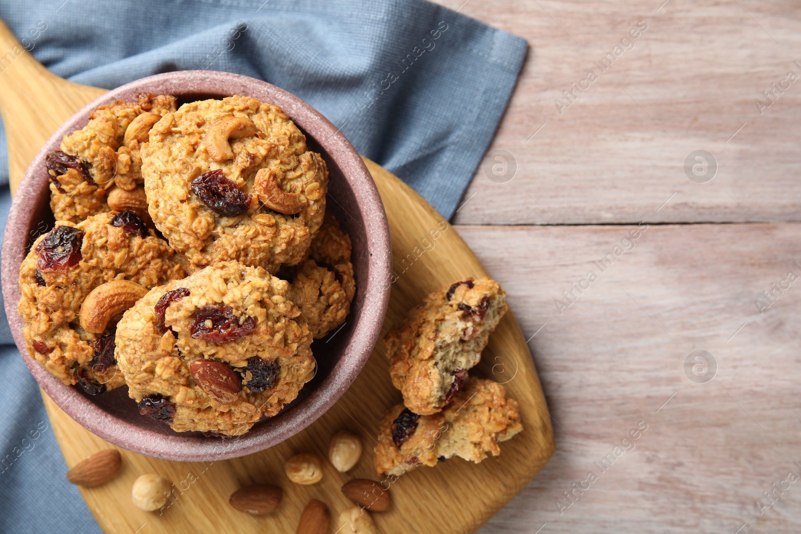 Photo of Delicious oatmeal cookies with raisins and nuts on wooden table, top view. Space for text