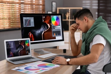 Tired retoucher at workplace with computer and laptop in office