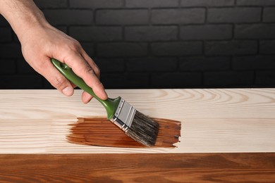 Photo of Man with brush applying walnut wood stain onto wooden surface, closeup