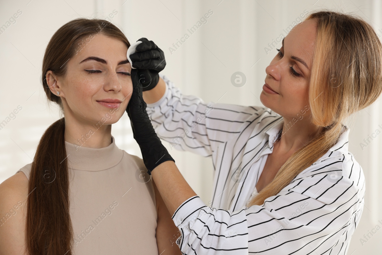 Photo of Beautician wiping client`s eyebrows after henna dyeing in salon