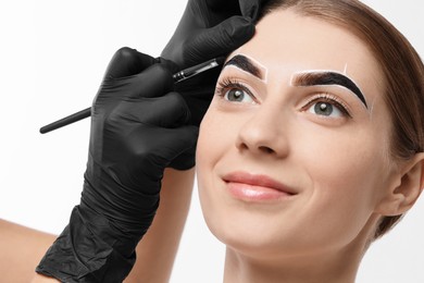 Young woman undergoing henna eyebrows dyeing procedure on light background, closeup