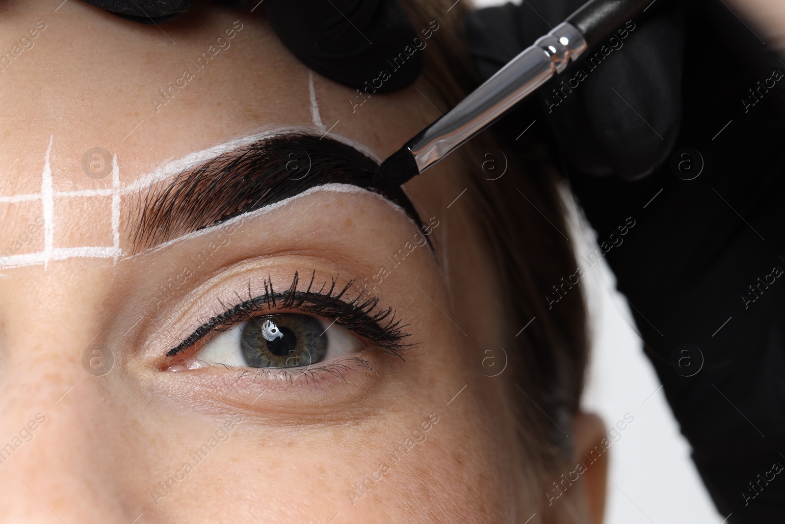 Photo of Young woman undergoing henna eyebrows dyeing procedure, closeup