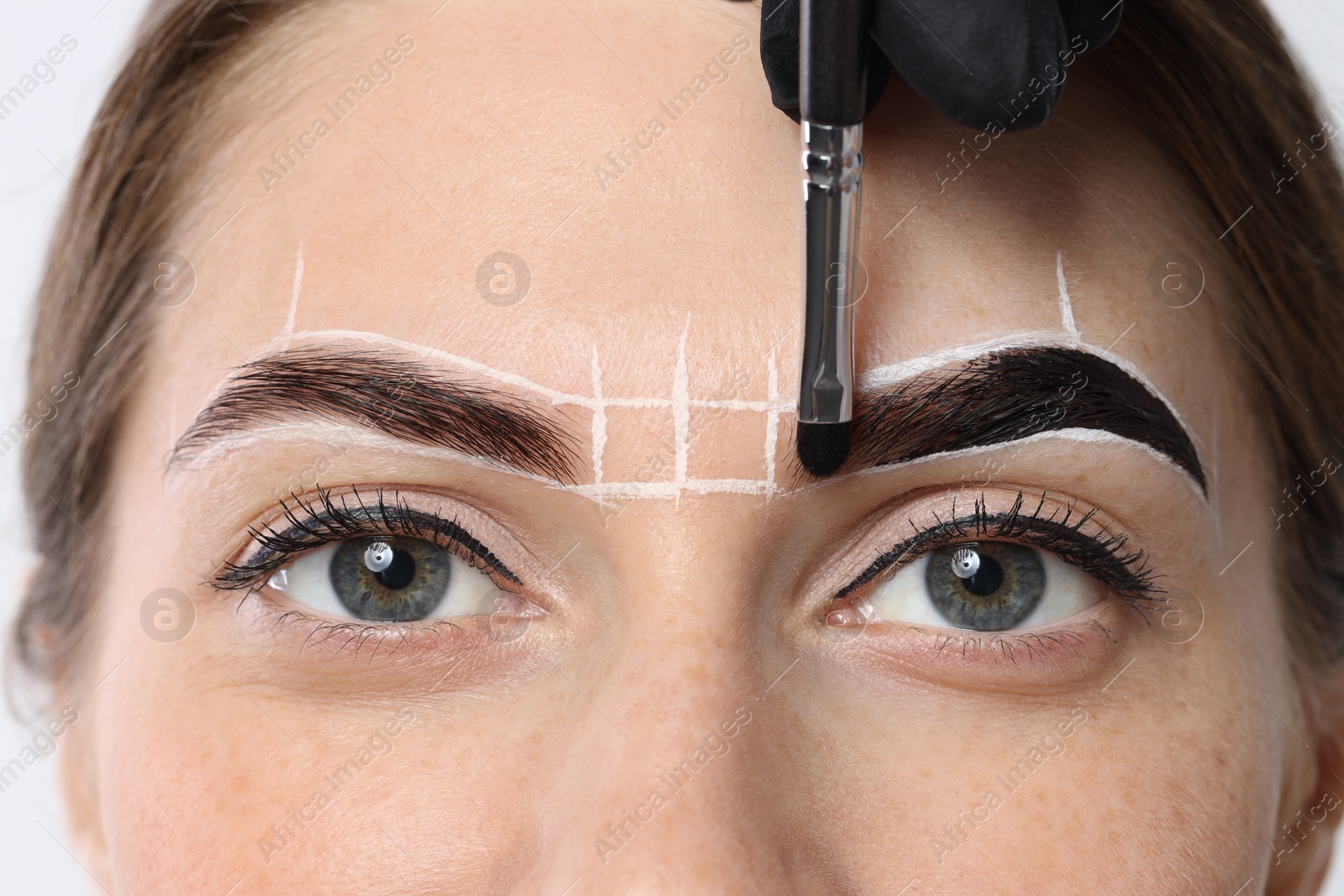 Photo of Young woman undergoing henna eyebrows dyeing procedure, closeup