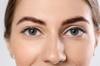 Beautiful young woman after henna eyebrows dyeing on light background, closeup