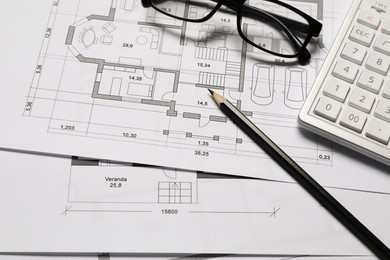 Photo of Different architectural drawings, calculator, glasses and pencil, closeup