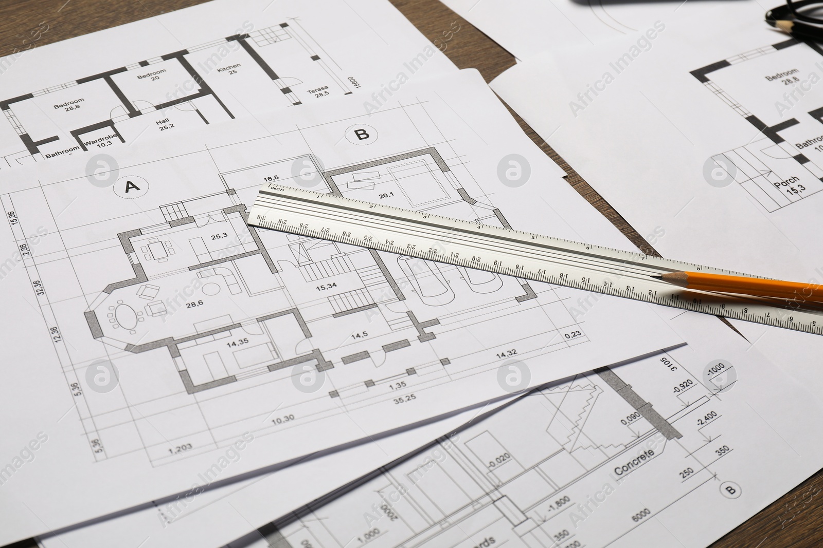 Photo of Different architectural drawings, ruler and pencil on wooden table, closeup