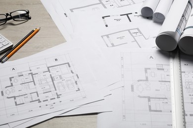 Photo of Different architectural drawings, glasses, ruler and pencils on wooden table, closeup