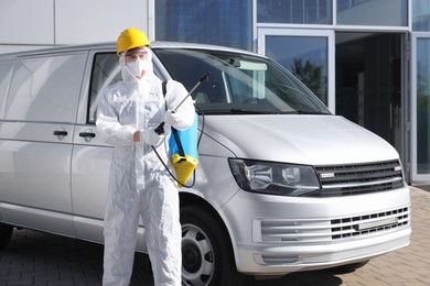 Photo of Pest control worker with spray tank near gray minibus outdoors