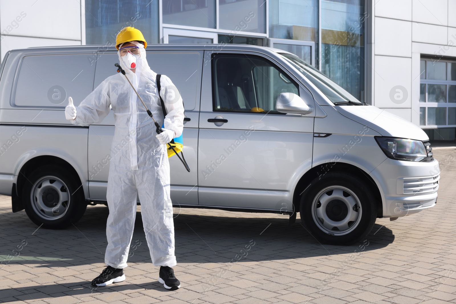 Photo of Pest control worker with spray tank showing thumbs up outdoors