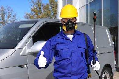 Photo of Pest control worker with spray tank showing thumbs up outdoors