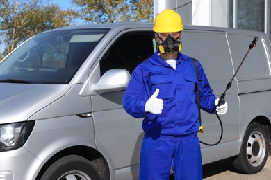 Photo of Pest control worker with spray tank showing thumbs up outdoors