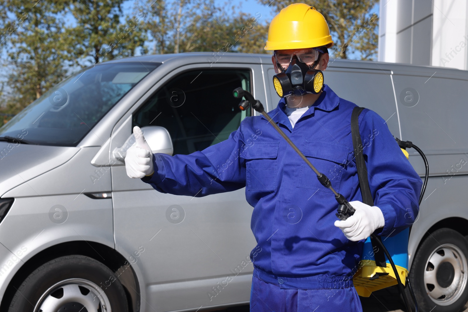 Photo of Pest control worker with spray tank showing thumbs up outdoors