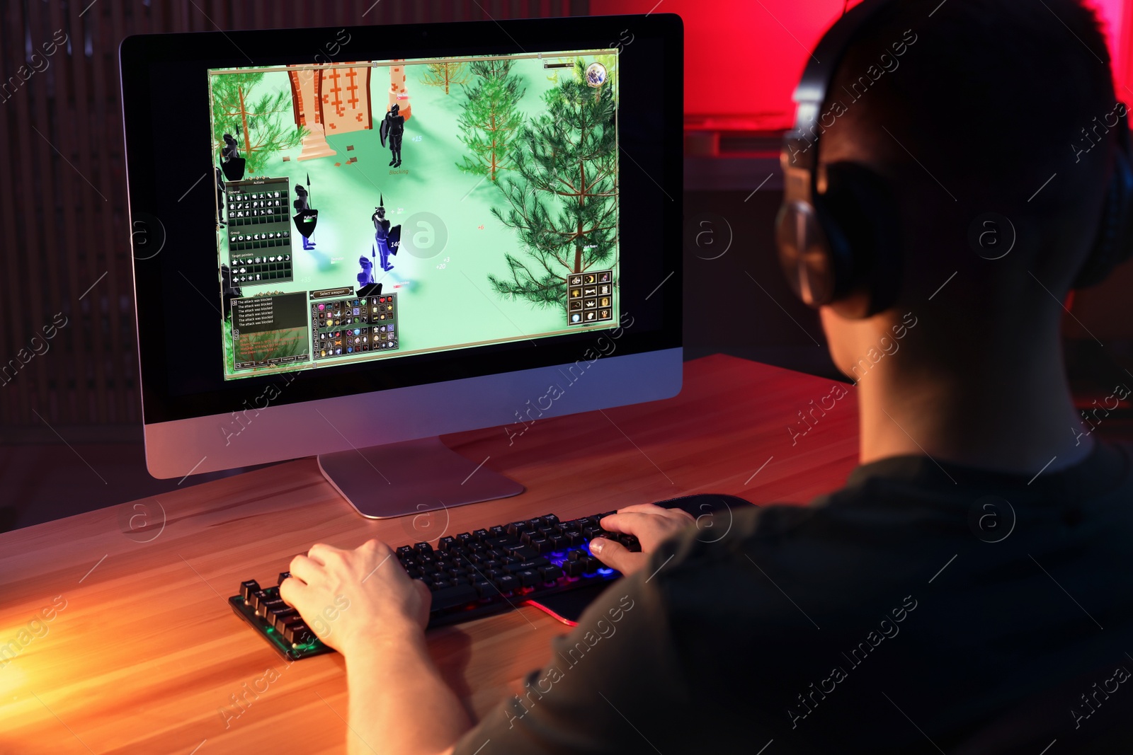 Photo of Young man playing video game with keyboard at wooden table indoors, back view