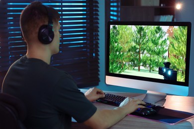 Young man playing video game with keyboard at wooden table indoors, back view