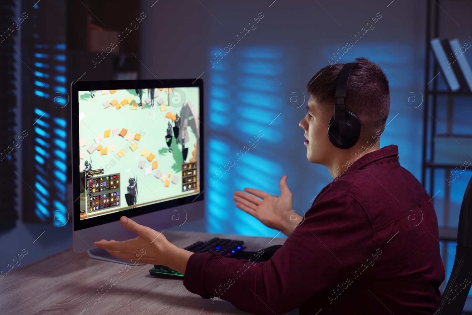 Photo of Emotional young man playing video game with keyboard at wooden table indoors