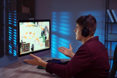 Emotional young man playing video game with keyboard at wooden table indoors